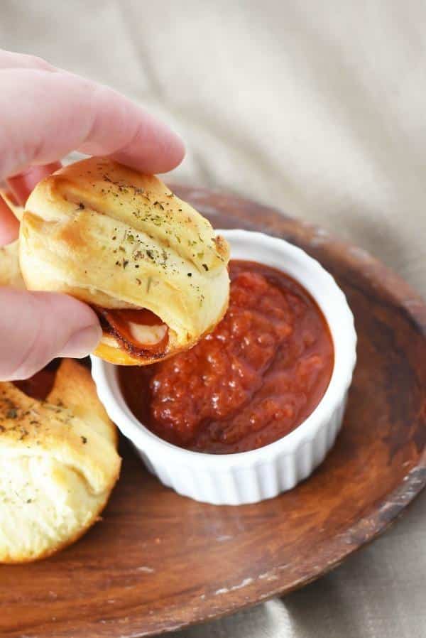 A hand dipping a pepperoni bomb into Ragu sauce. 