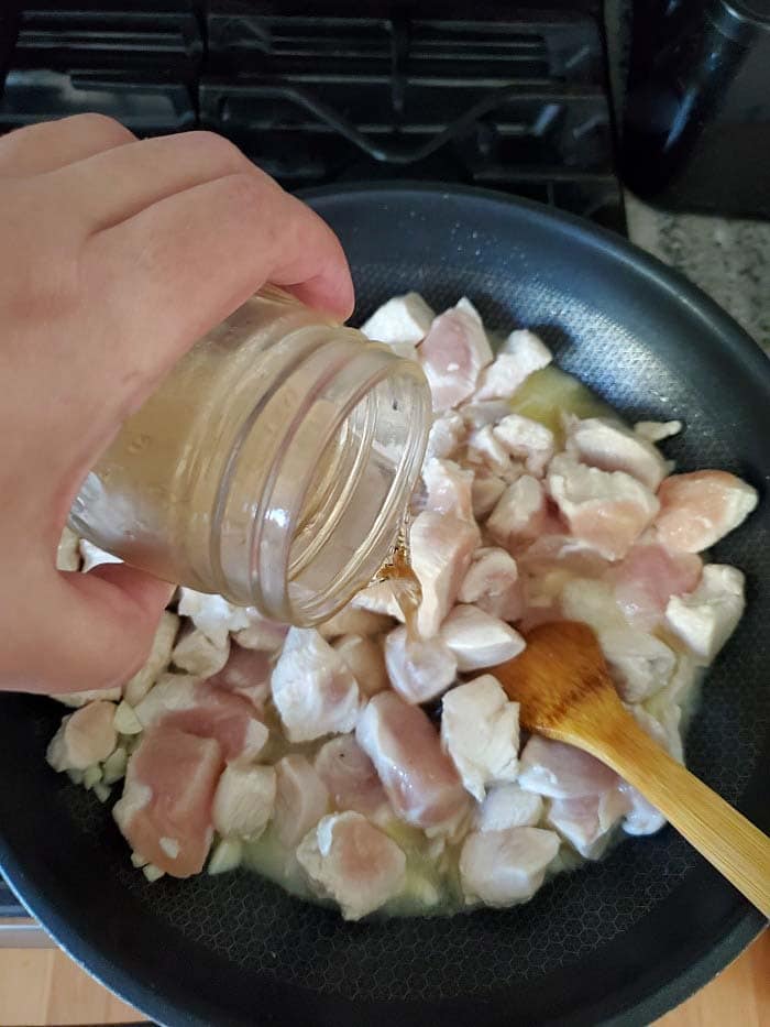 hand pouring wine into a skillet with chicken cubes