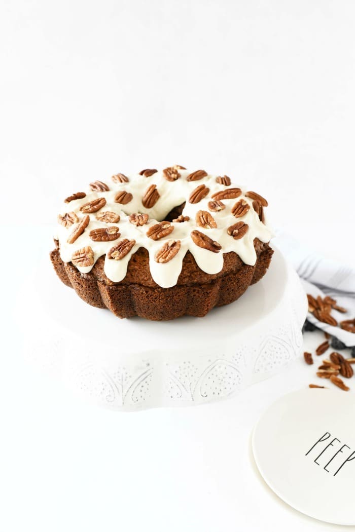 cream cheese frosted carrot cake topped with halved walnuts on a white cake stand.