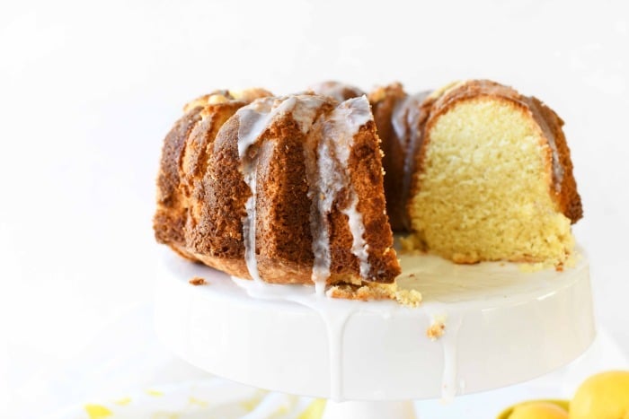 lemon bundt cake with a slice missing on a white cake stand. 