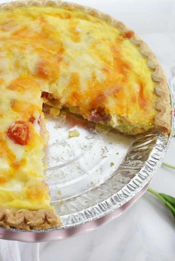 Baked Cheesy ham, tomato, and potato quiche with one slice removed.