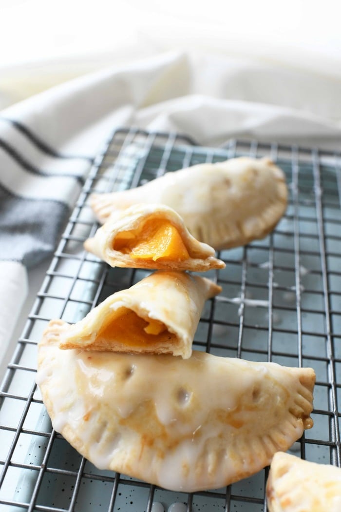 Iced peach hand pies on cooling rack with one pie broken in half to show the peaches inside. 