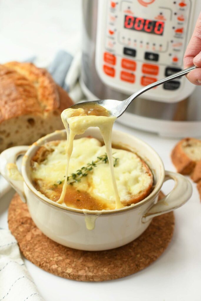 Cheesy French Onion soup on a spoon with a cheese pull.