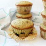 Bakery style zucchini muffins stacked on a white table.