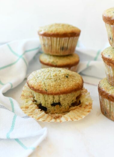 Bakery style zucchini muffins stacked on a white table.