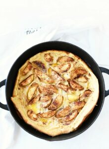 baby apple pancake in cast iron pan on a white table.