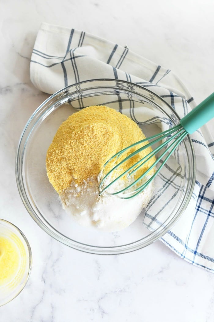 corn muffin mix in a glass bowl with a blue whisk and checkered napkin.
