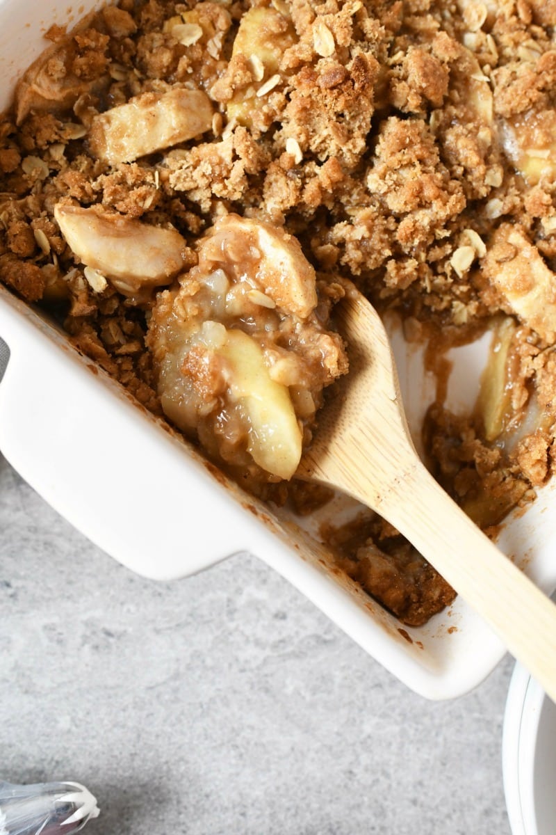Apple Crisp in a white squared pan with a wooden spoon.