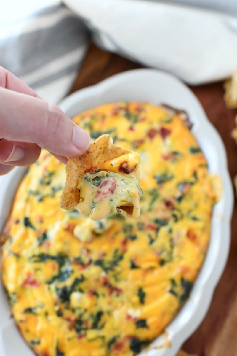 Cheesy Spinach Dip. A chip is dipped and a hand is holding it.