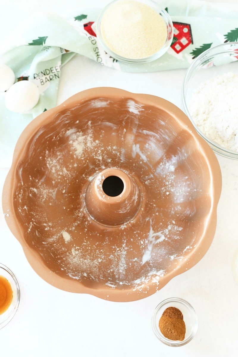 Greased cooper bundt pan on a white table with ingredients and a mint green holiday napkin.