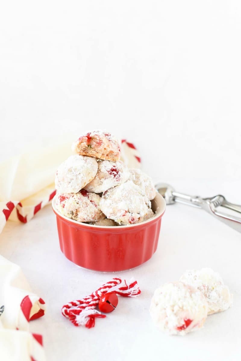 Snowball cherry cookies in a red bowl with a cookie scooper.