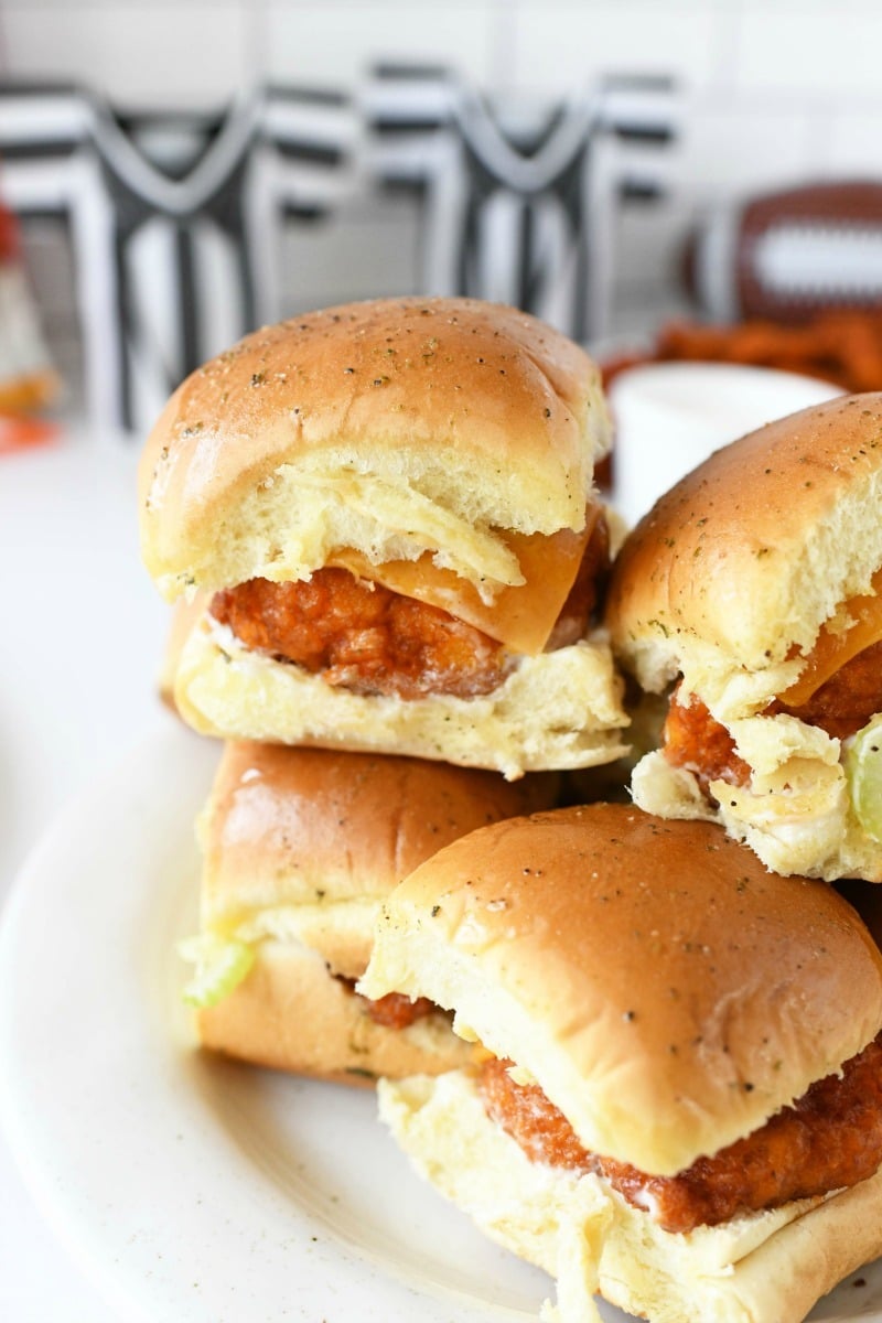 Buffalo Chicken Sliders stacked on a white plate. There are black and white referee cozies in the background.