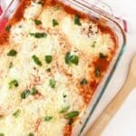 Ravioli Lasagna Recipe baked in a deep dish Pyrex. There is a red checkered napkin and a wooden spoon in the image.