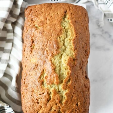 Sour Cream Banana Bread Recipe. A fully baked banana bread loaf is on a marble table with a fringe napkin.
