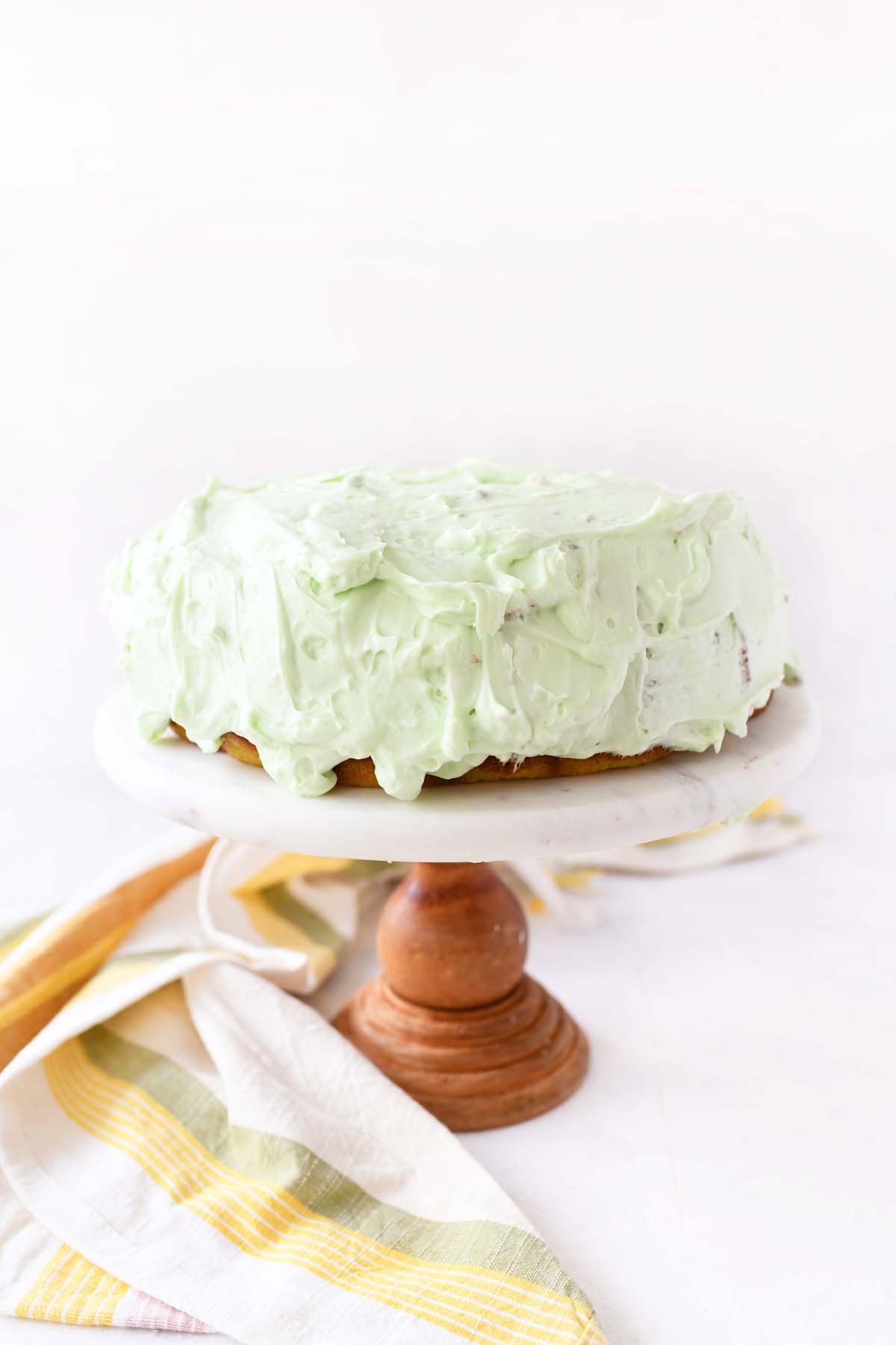 Frosted pistachio cake on a marble cake stand.