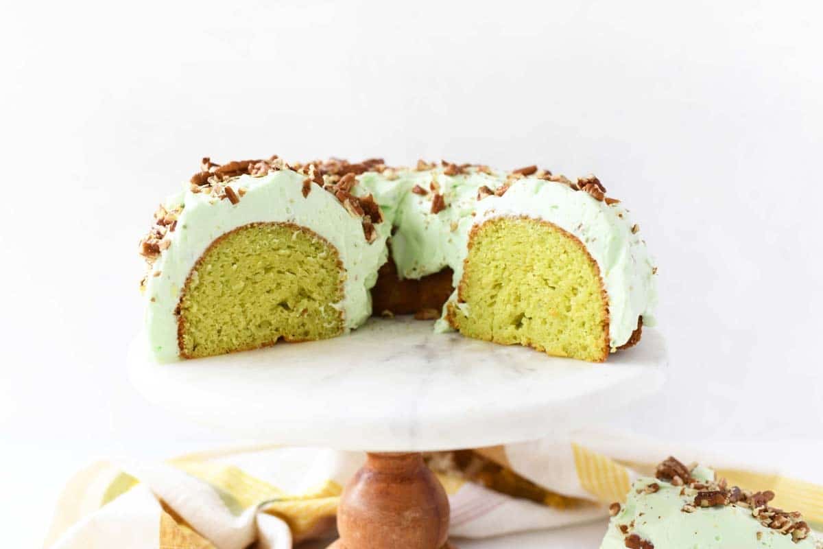 Pistachio pudding bundt cake slice on a white marble cake stand.
