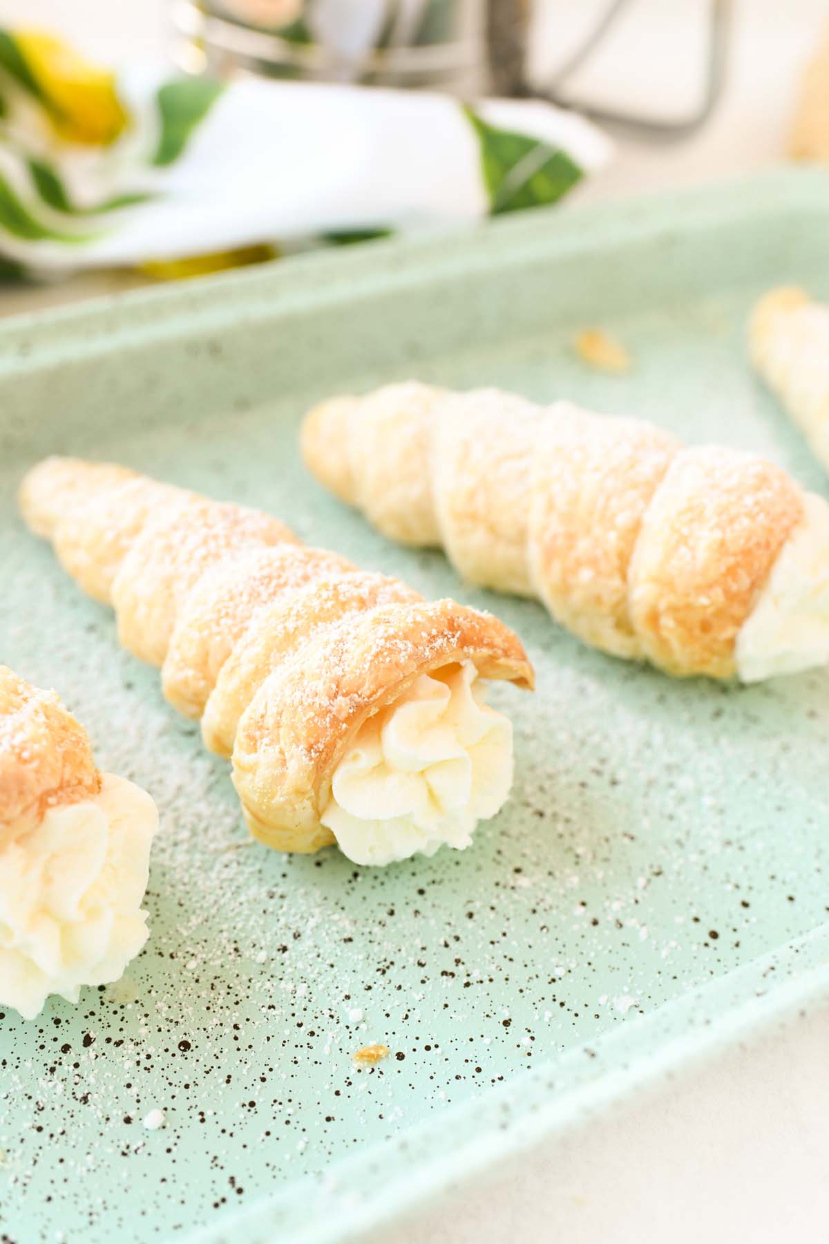 Cream filled Cream Horns with powdered sugar on a blue pan.