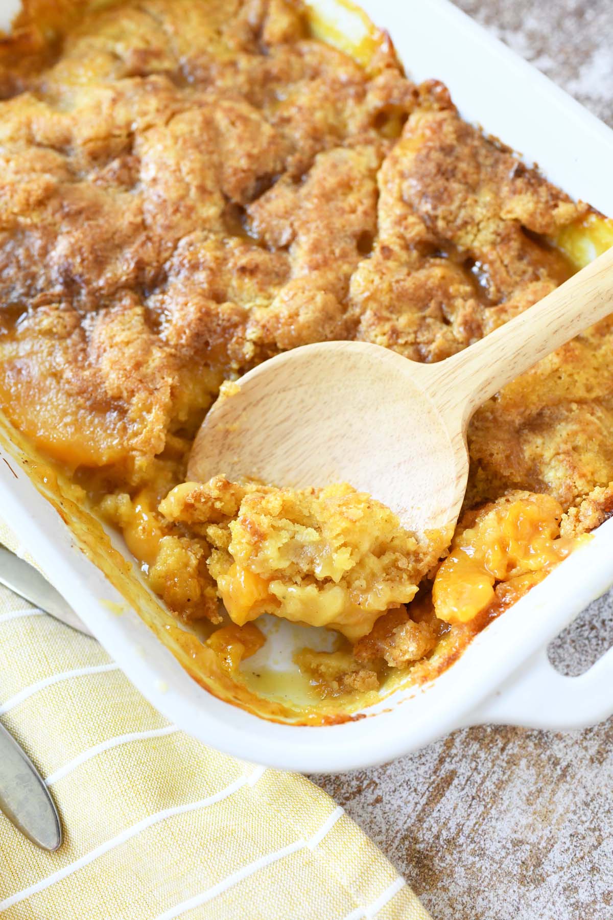 Canned peaches dump cake in a white pan with a wooden spoon.