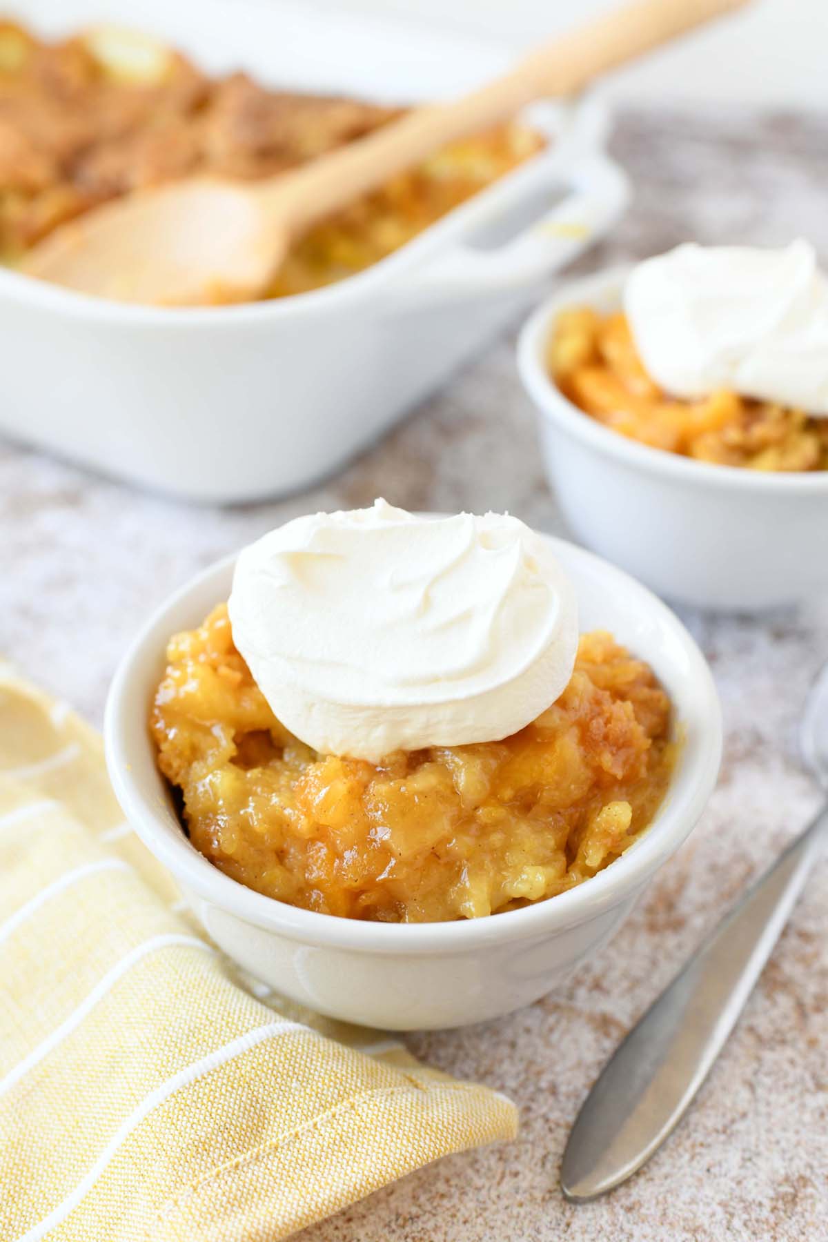 A white bowl of peach dump cake with whipped topping.