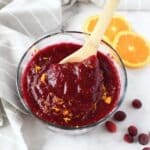 Homemade cranberry sauce in a glass bowl with orange zest and a spoon.
