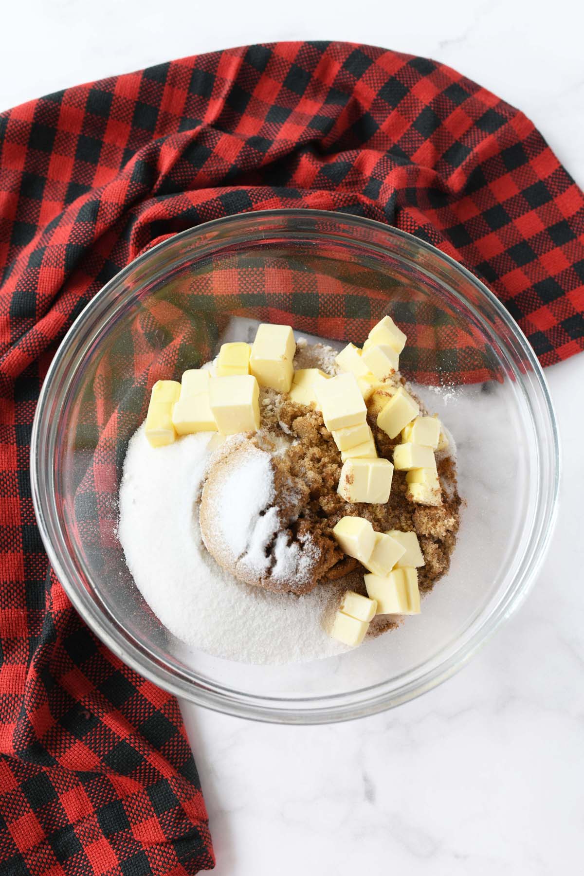 Butter cubes and sugar in a glass bowl with a plaid napkin.