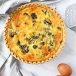 A baked caramelized onion and mushroom quiche with a grey napkin.