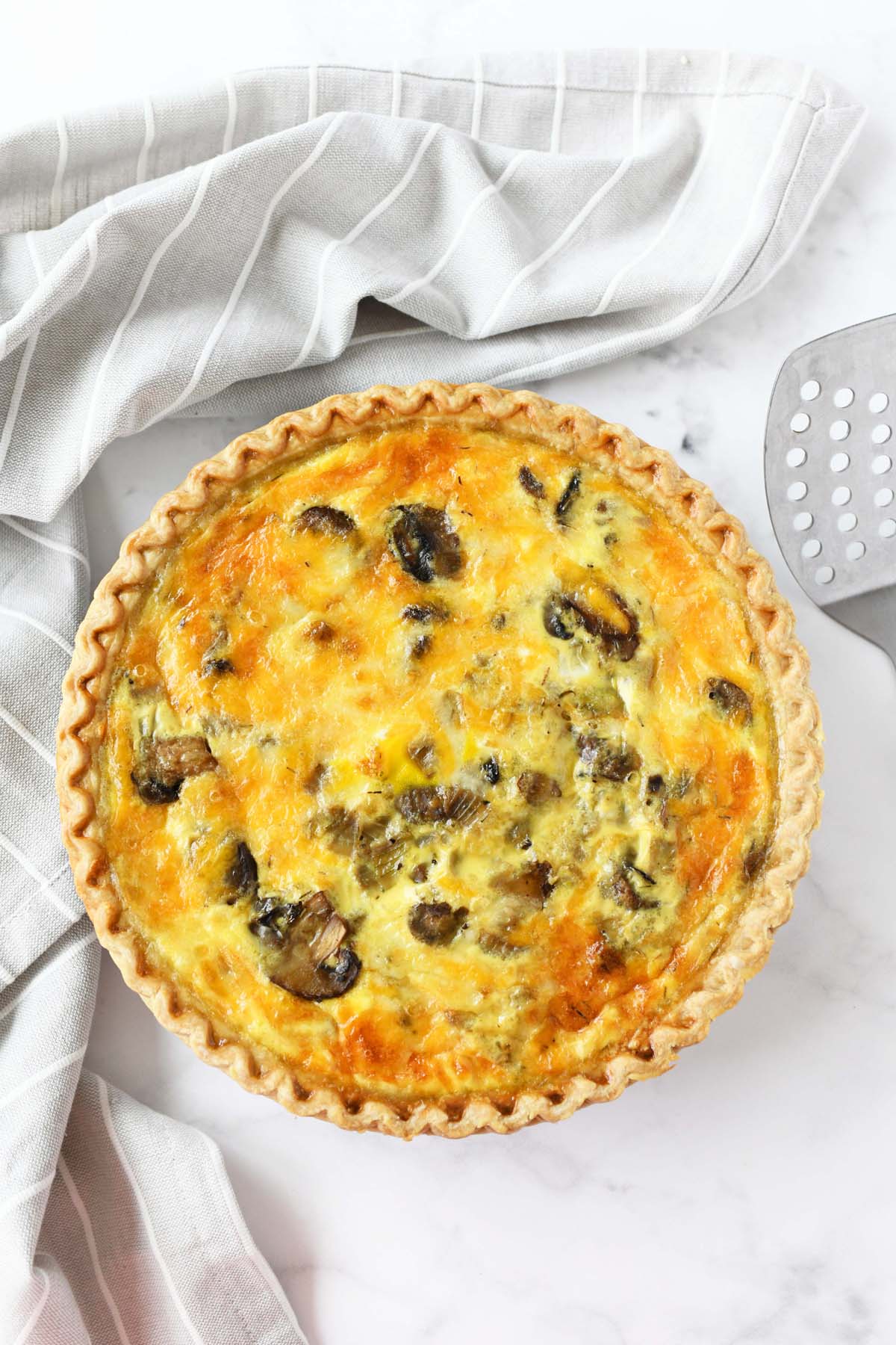A baked caramelized onion and mushroom quiche on a white table.