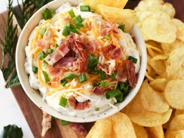 Loaded creamy chip dip in a white bowl with bacon, and cheese.