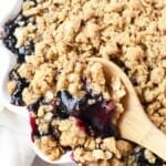 Golden brown Blueberry Crisp with a wooden spoon.