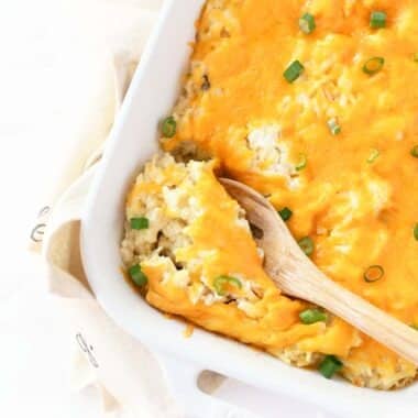 A wooden spoon nestled in cheesy hash brown casserole.