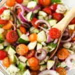 Colorful cucumber and tomato salad in a glass bowl with a wooden spoon.