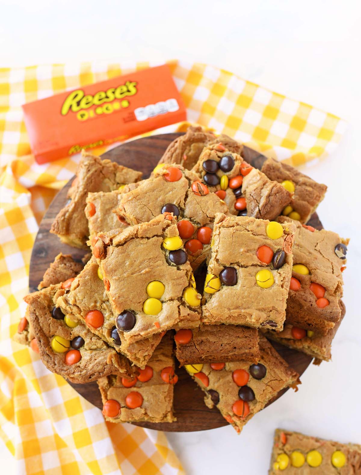 Reese's brownies stacked on a wooden platter with a yellow checkered napkin.