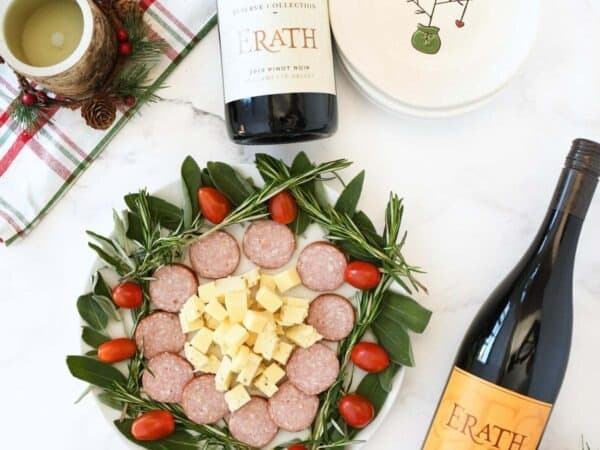 Holiday meat and cheese snack plate near wine bottles.