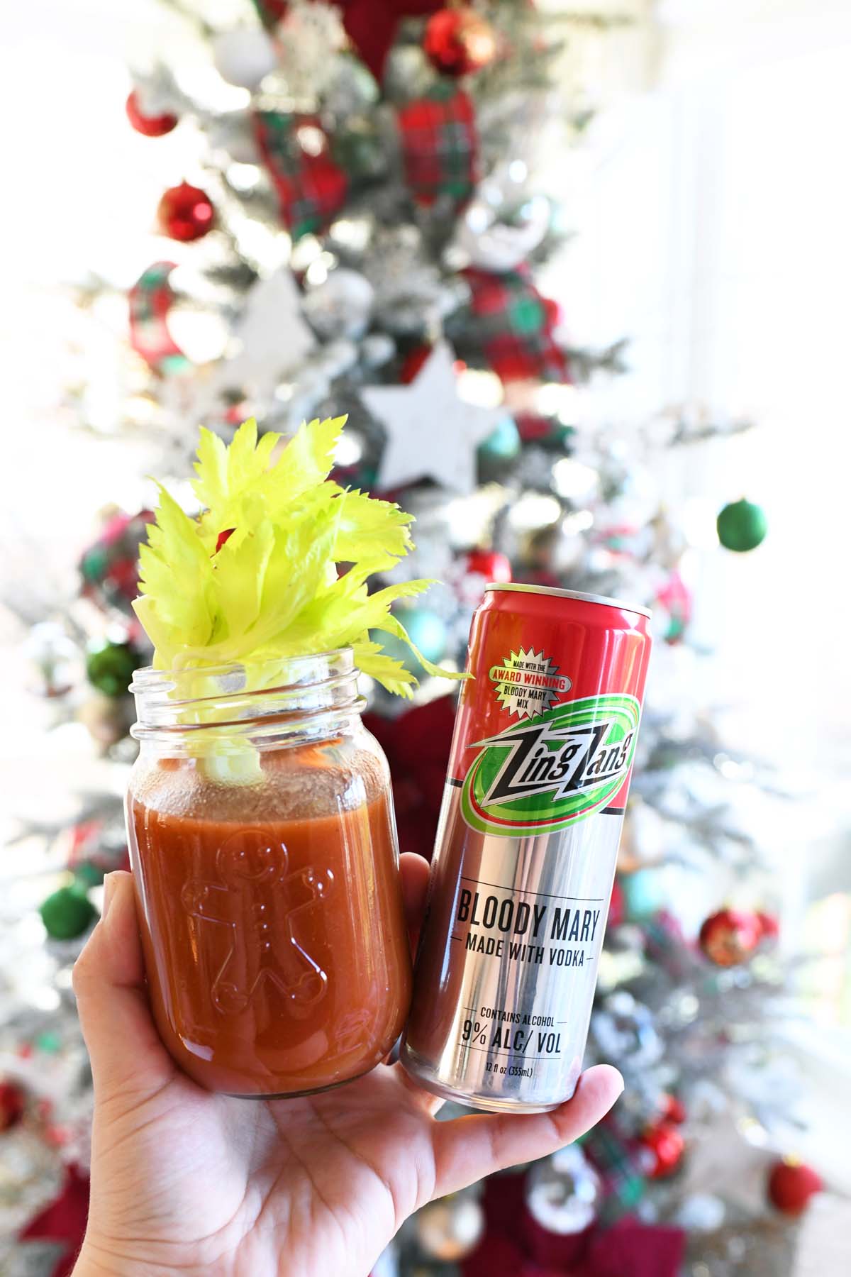 A hand holiday a bloody Mary in front of a tree.