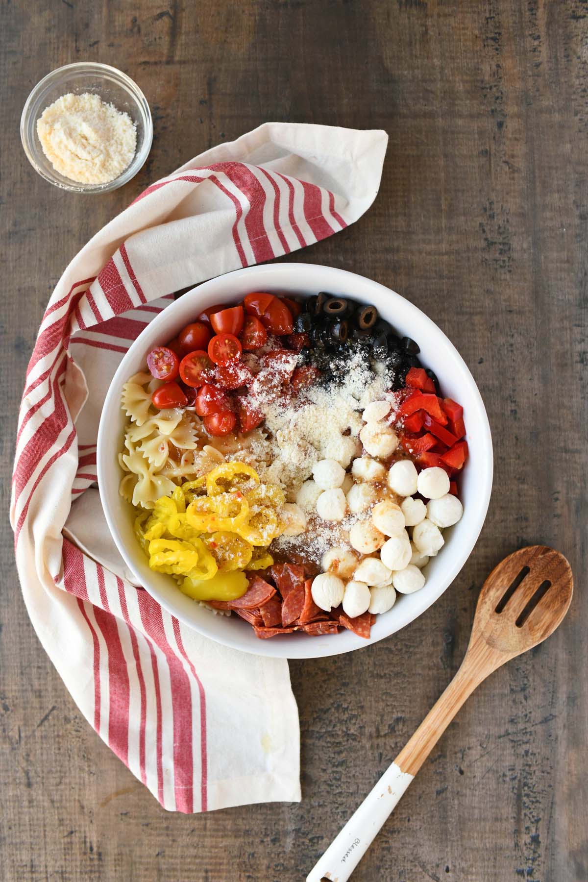 Unmixed pizza pasta salad in a white bowl near a red striped napkin. 