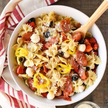 Colorful pizza pasta salad in a white bowl with a wooden spoon.