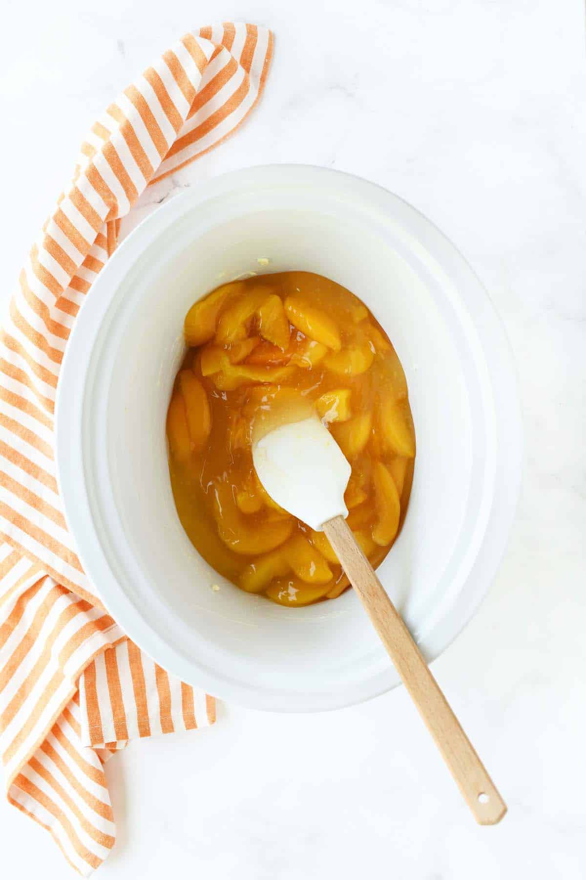 Canned peaches in a white slow cooker insert. 