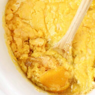Peach cobbler in a white slow cook and wooden spoon.