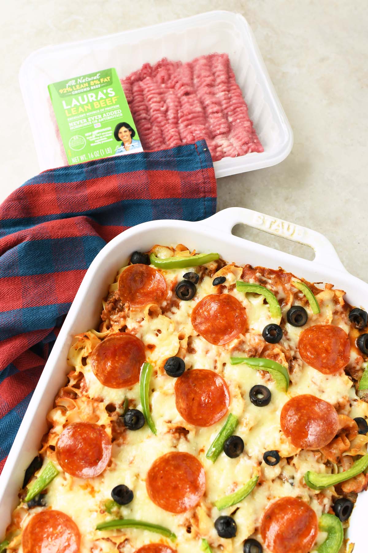 A cheesy and beefy baked pizza casserol near a package of Laura's Lean ground beef.