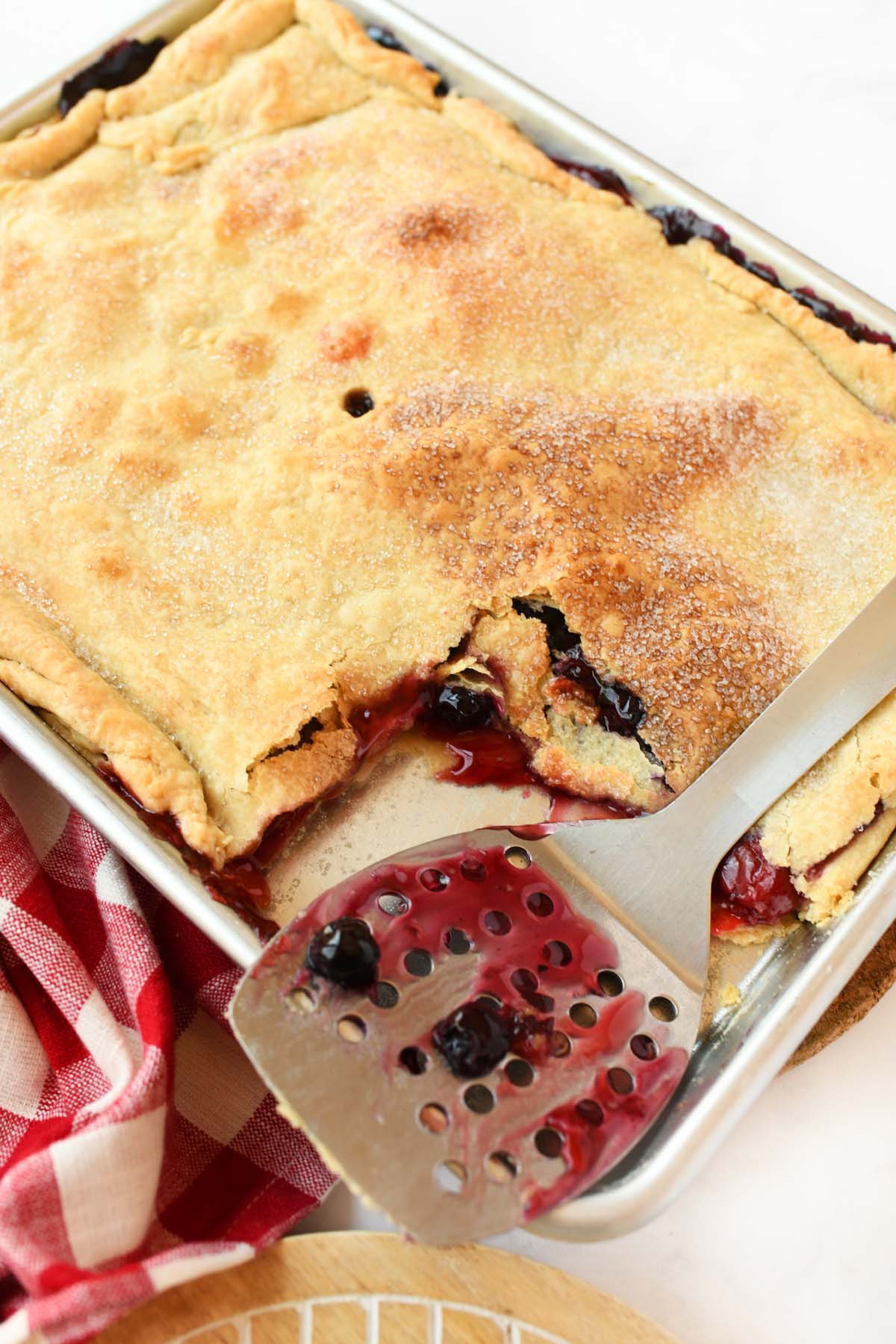 Berry stained spatula near a sheet pan pie.