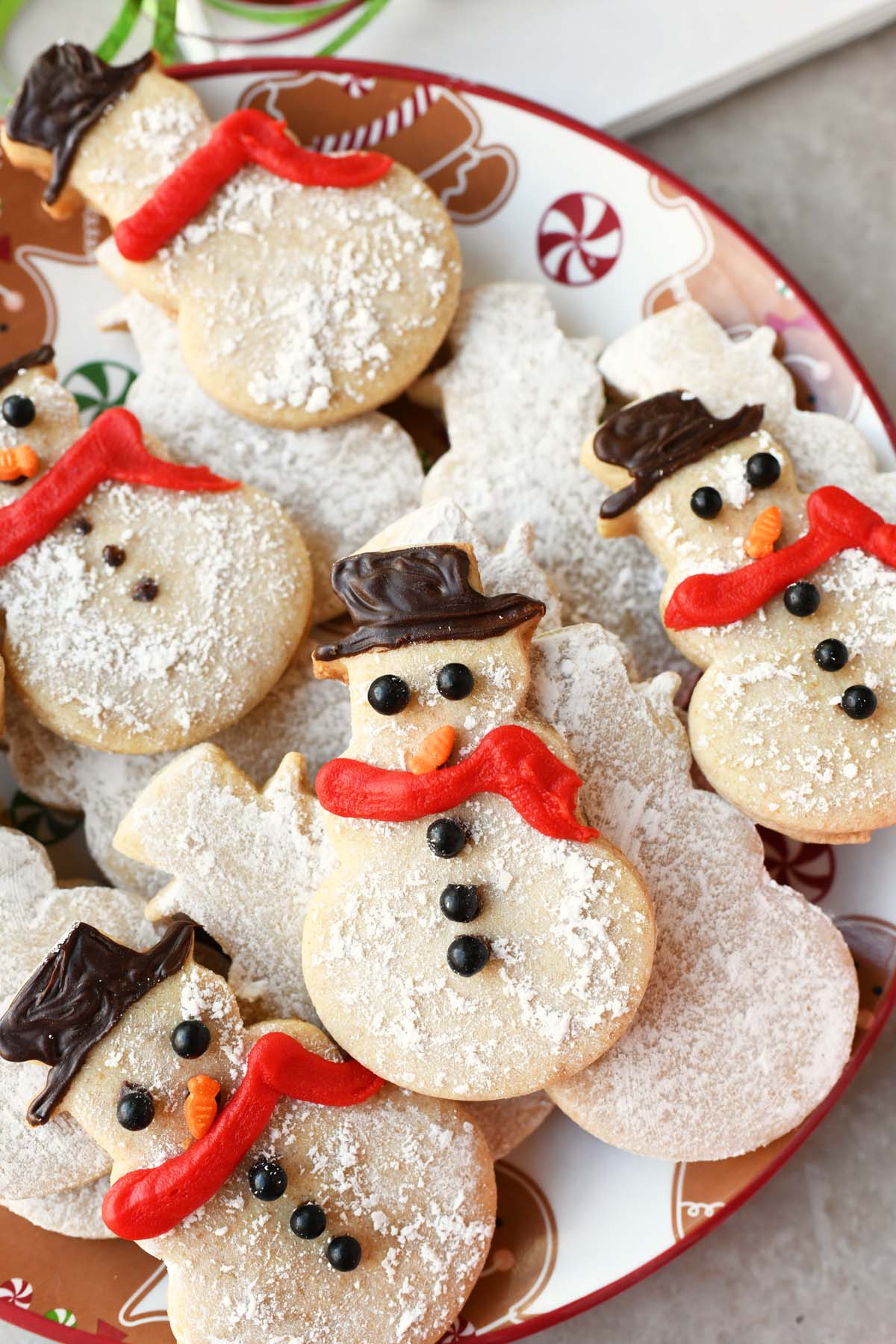 A plate of decorated snowman cookies with red scarves and black hats.