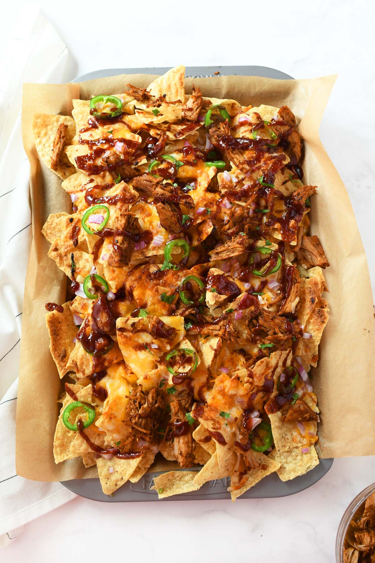 A pan of cheesy, bbq sauce topped pulled pork nachos.