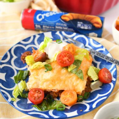 Crescent Roll taco bake portion on a blue plate with colorful toppings.