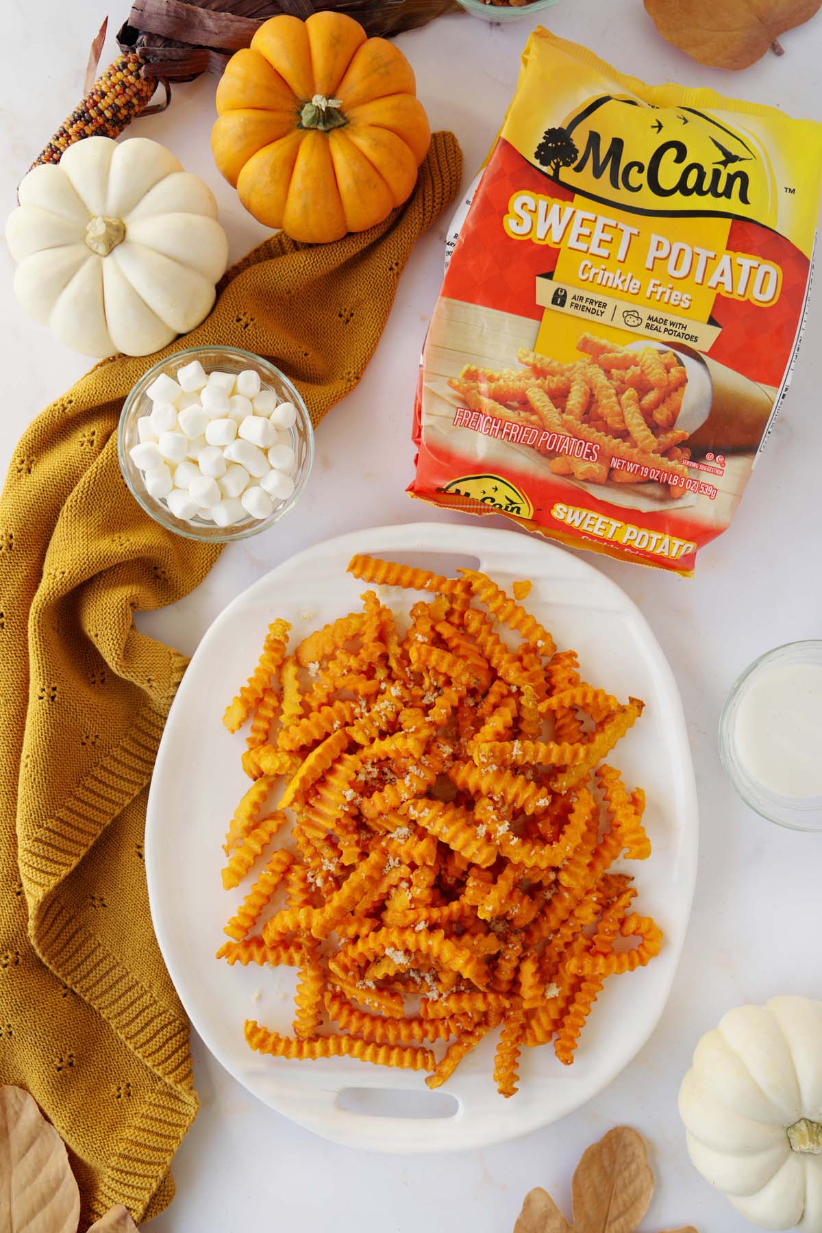 A platter of McCain Sweet Potato Crinkle fries near mini pumpkins, ingredients, and a McCain's Sweet Potato fry bag.