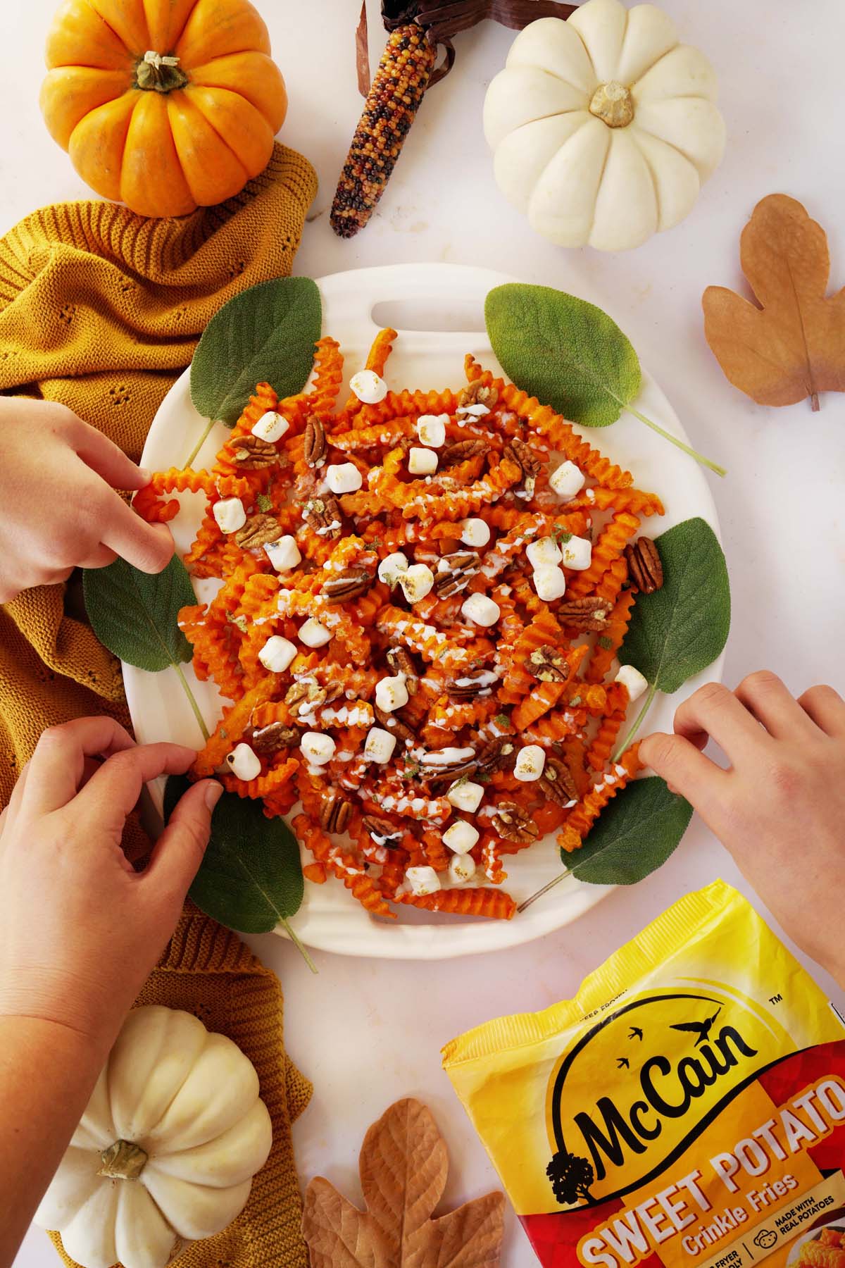 Hands grabbing loaded sweet potato fries on a harvest themed table.