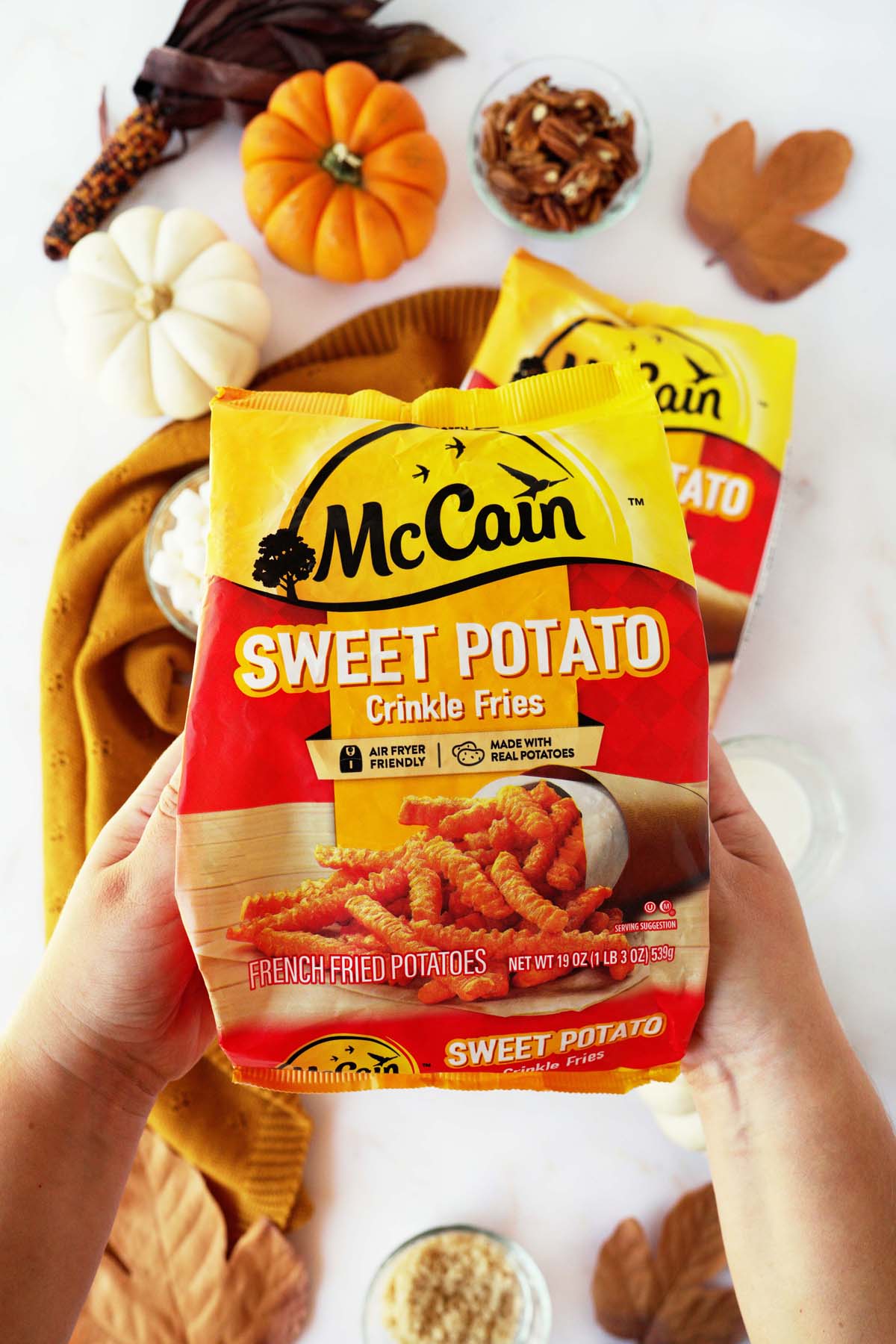 Hands holding up a red and yellow McCain Sweet Potato French Fries Bag.