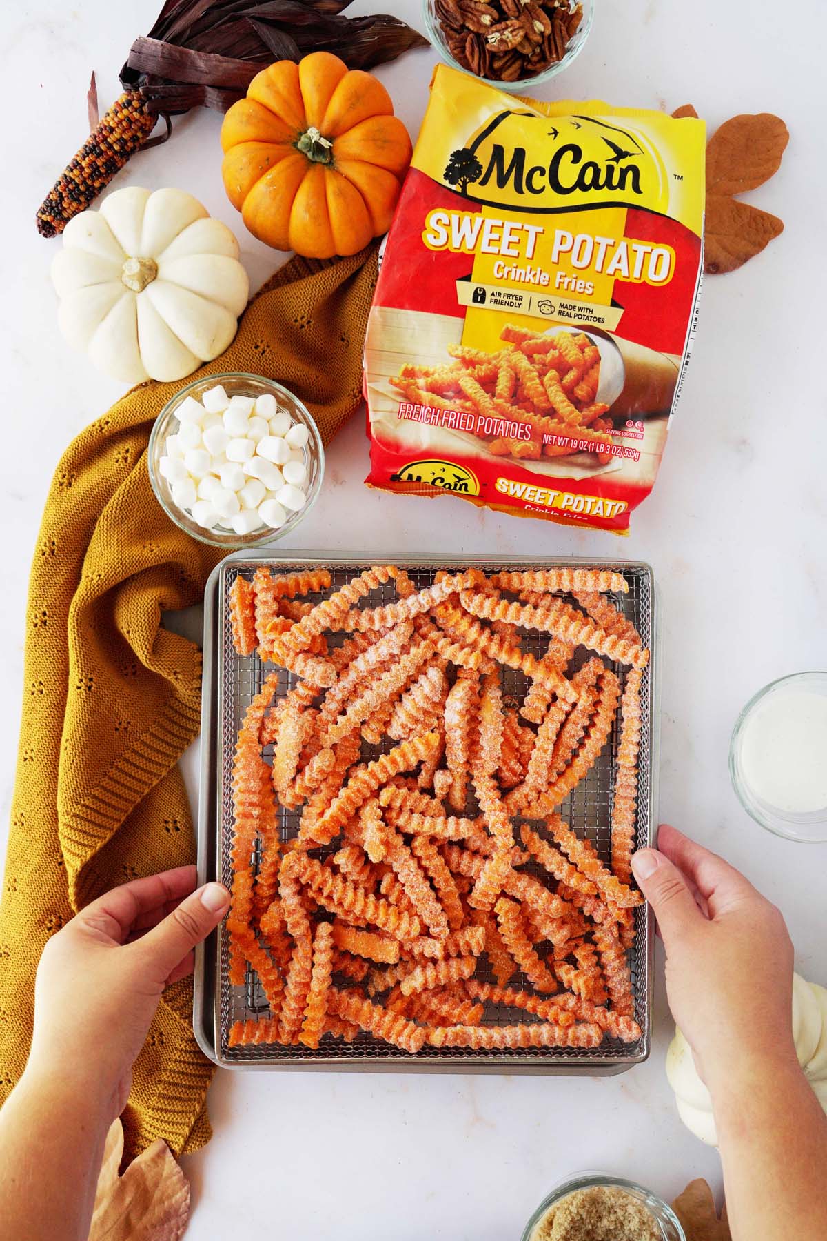 A hand holding up McCain Sweet Potato crinkle fries on a silver air fryer tray.