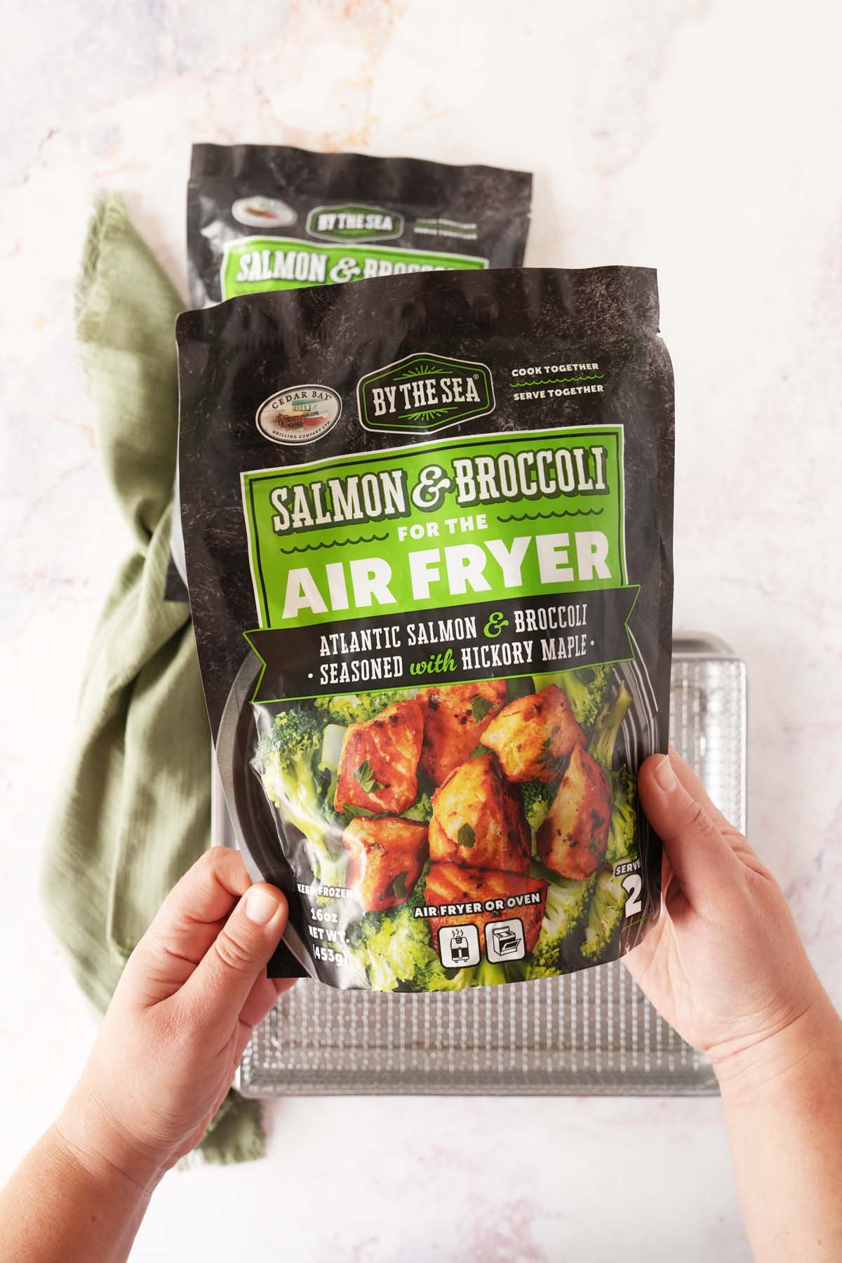 A hand holding a bag of salmon and broccoli for the air fryer.