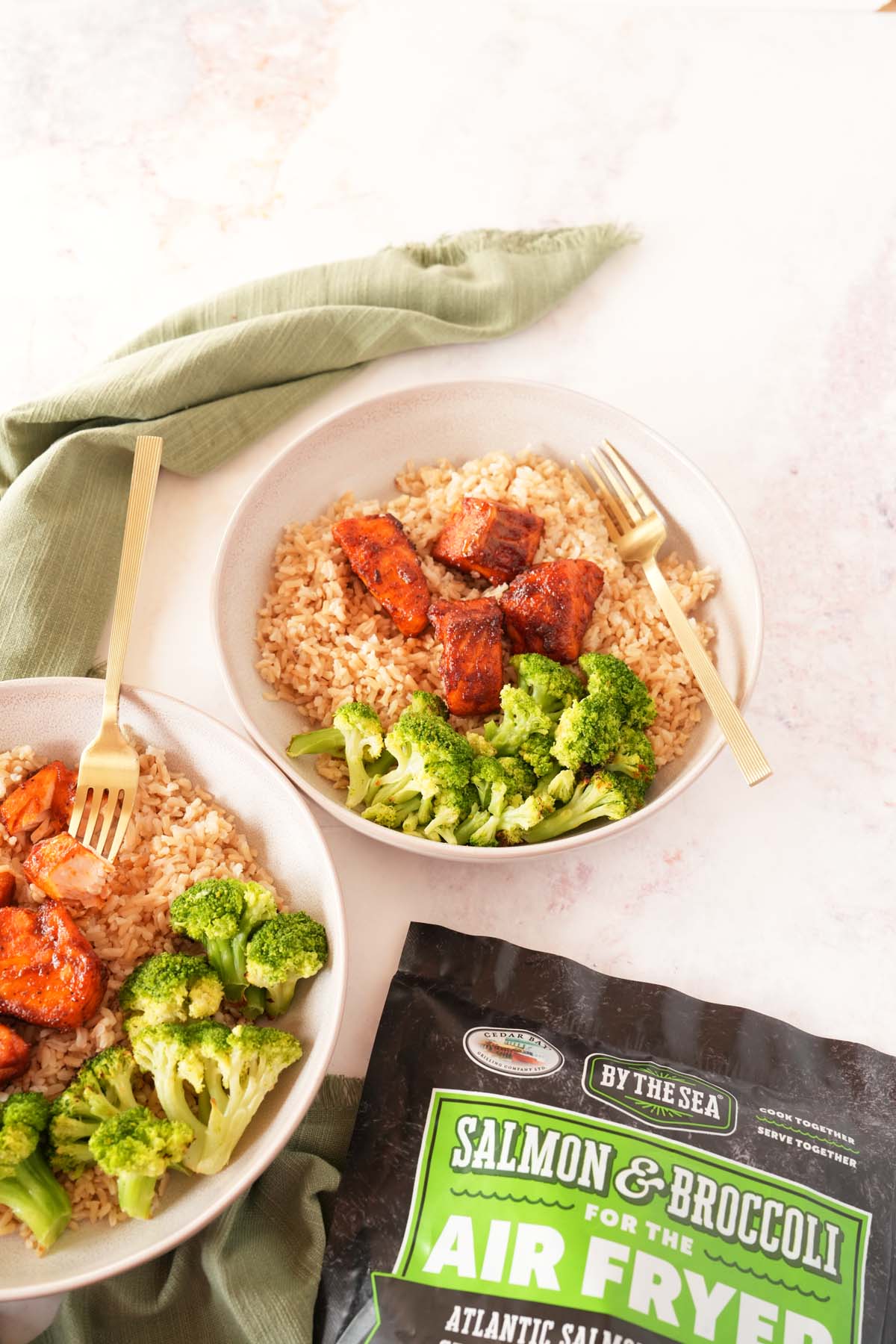 A plate of salmon and broccoli near a green napkin and product bag.