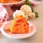 Cherry cake slice on pink plate with flowers, and whole cake in the background.